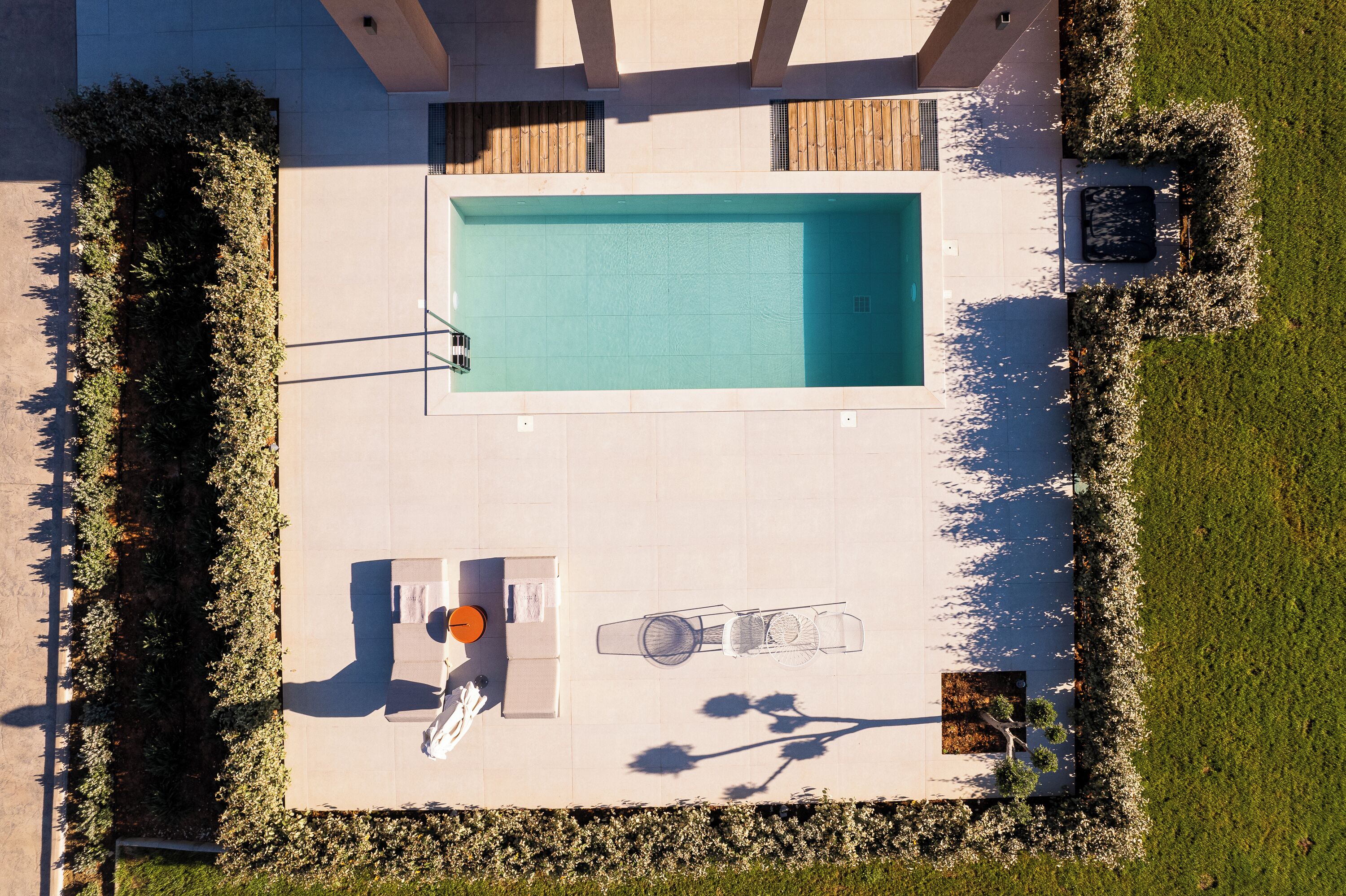Vista aérea de un moderno espacio exterior con piscina, una tumbona, una pequeña mesa con una bebida y una zona de estar con sombrillas.