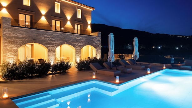 Un área de piscina moderna con fachada de piedra, asientos al aire libre e iluminación ambiental.