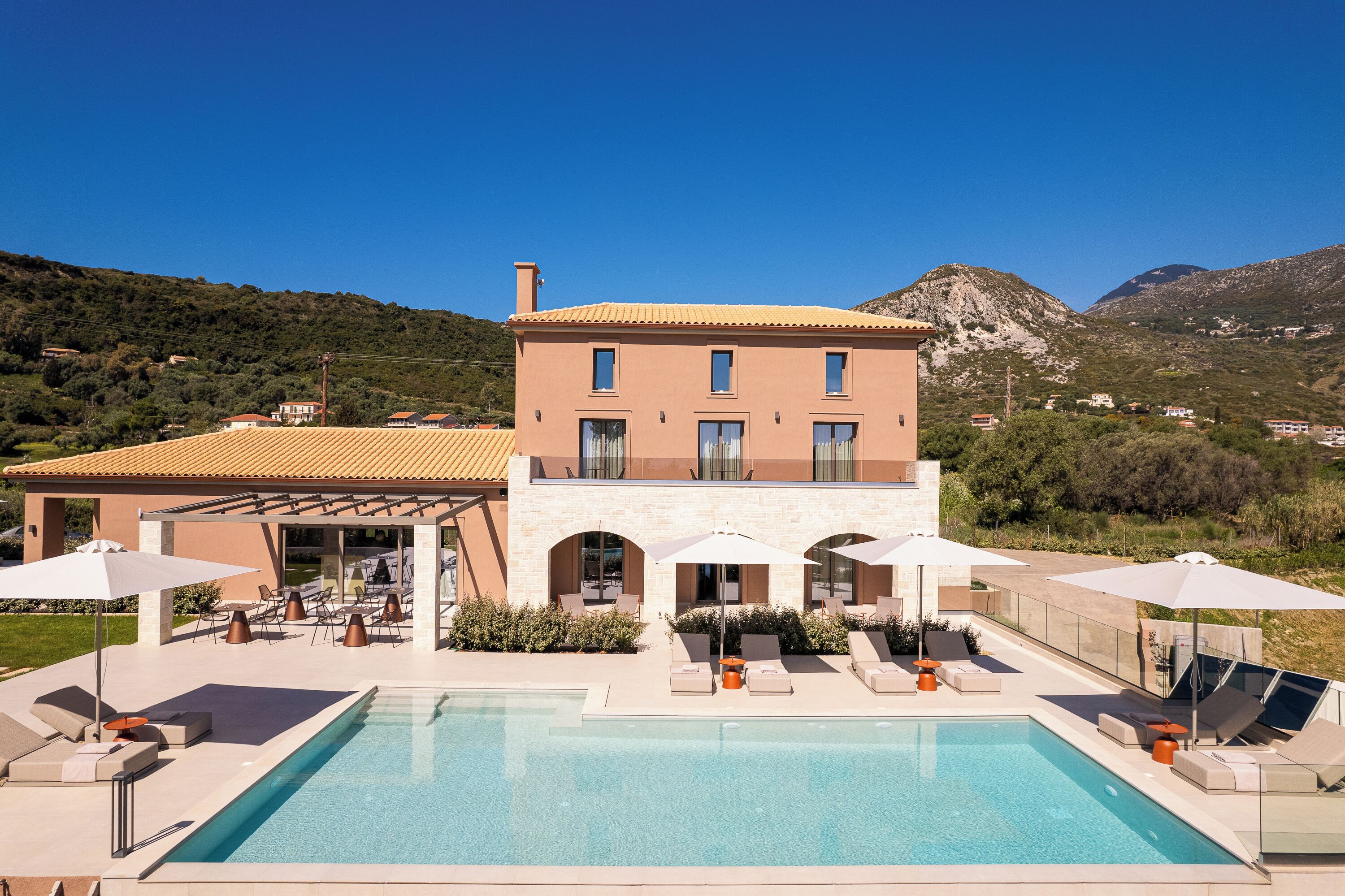 A two-story building with a swimming pool, outdoor seating, and a view of the surrounding hills.