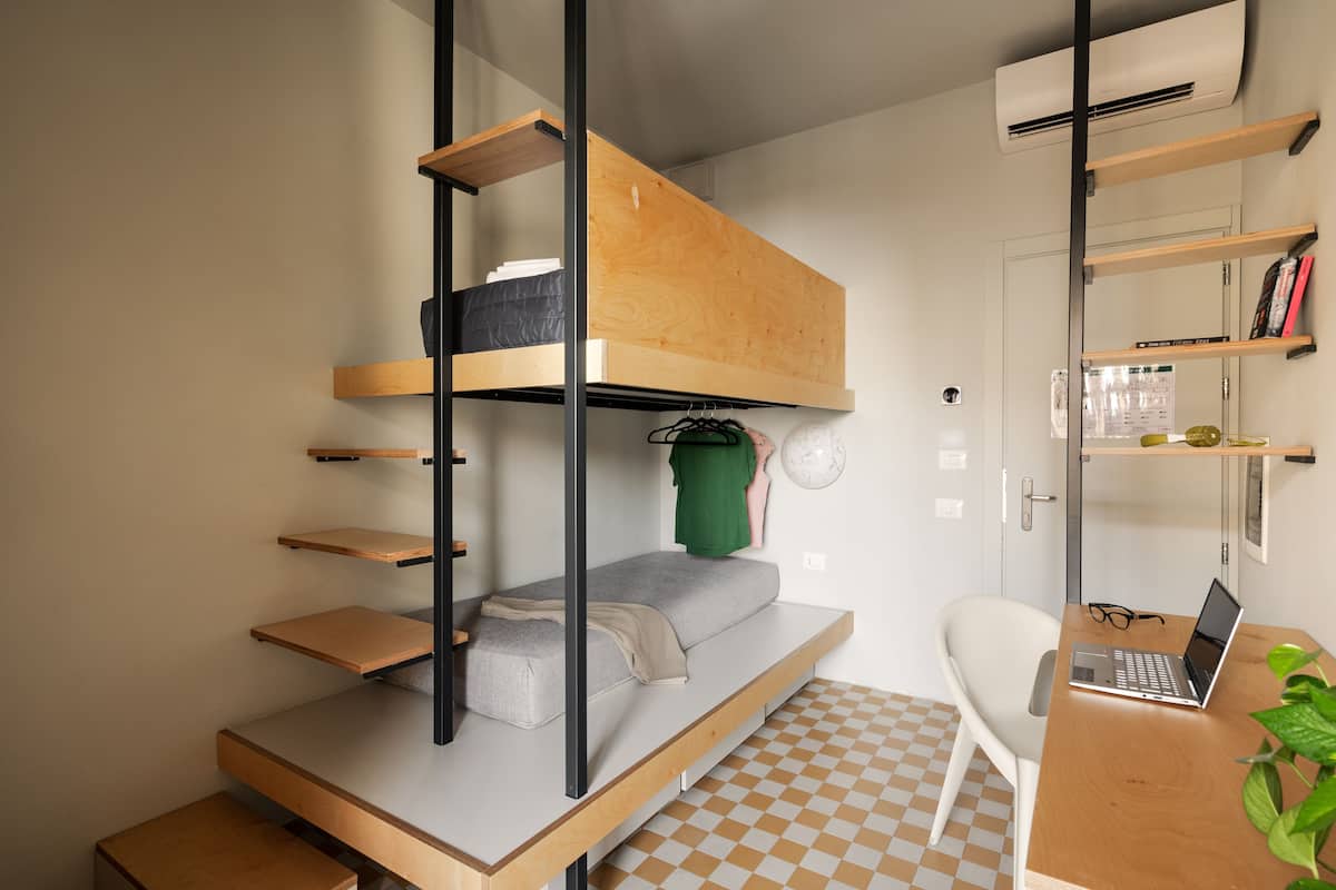 A compact room with a bunk bed, a desk with a laptop, and a chair.