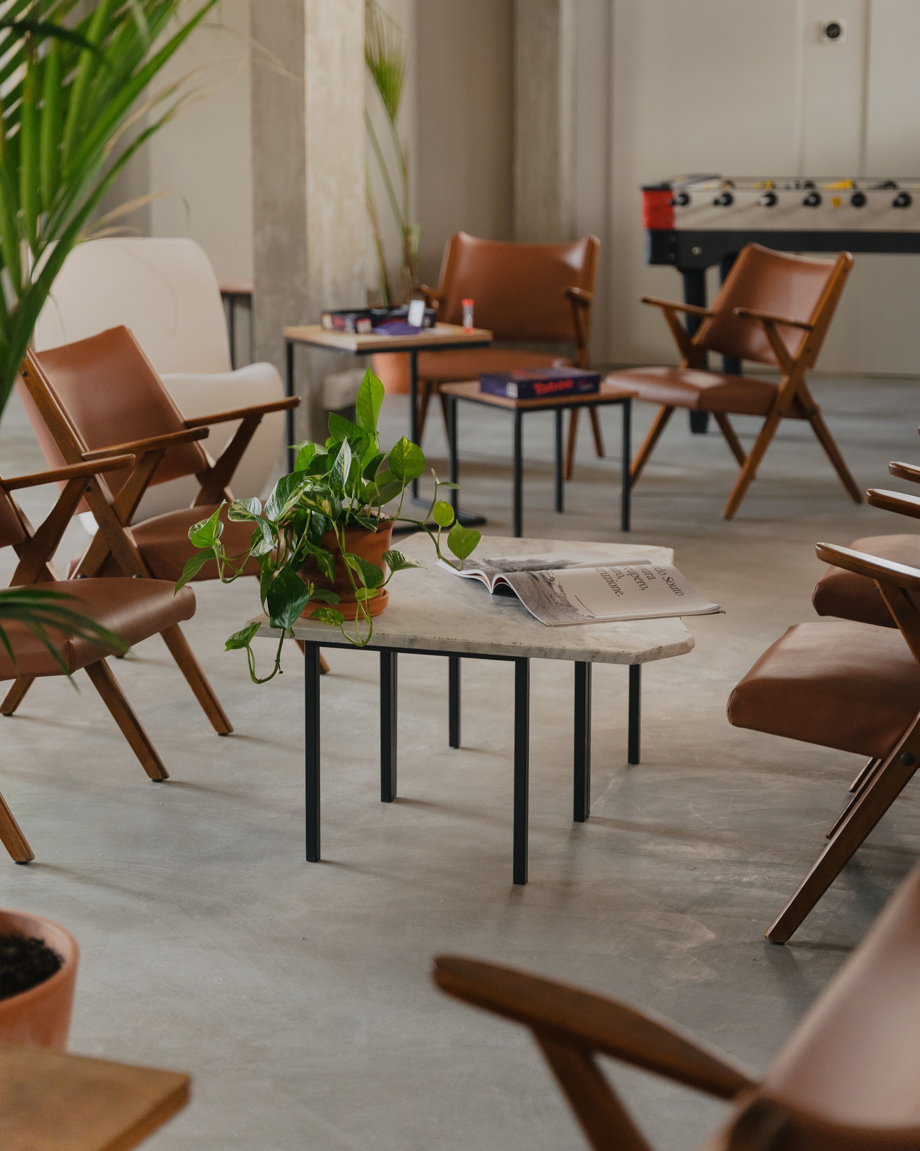 Un área de estar moderna con sillones de cuero, una mesa de fútbol y una mesa baja con una planta.