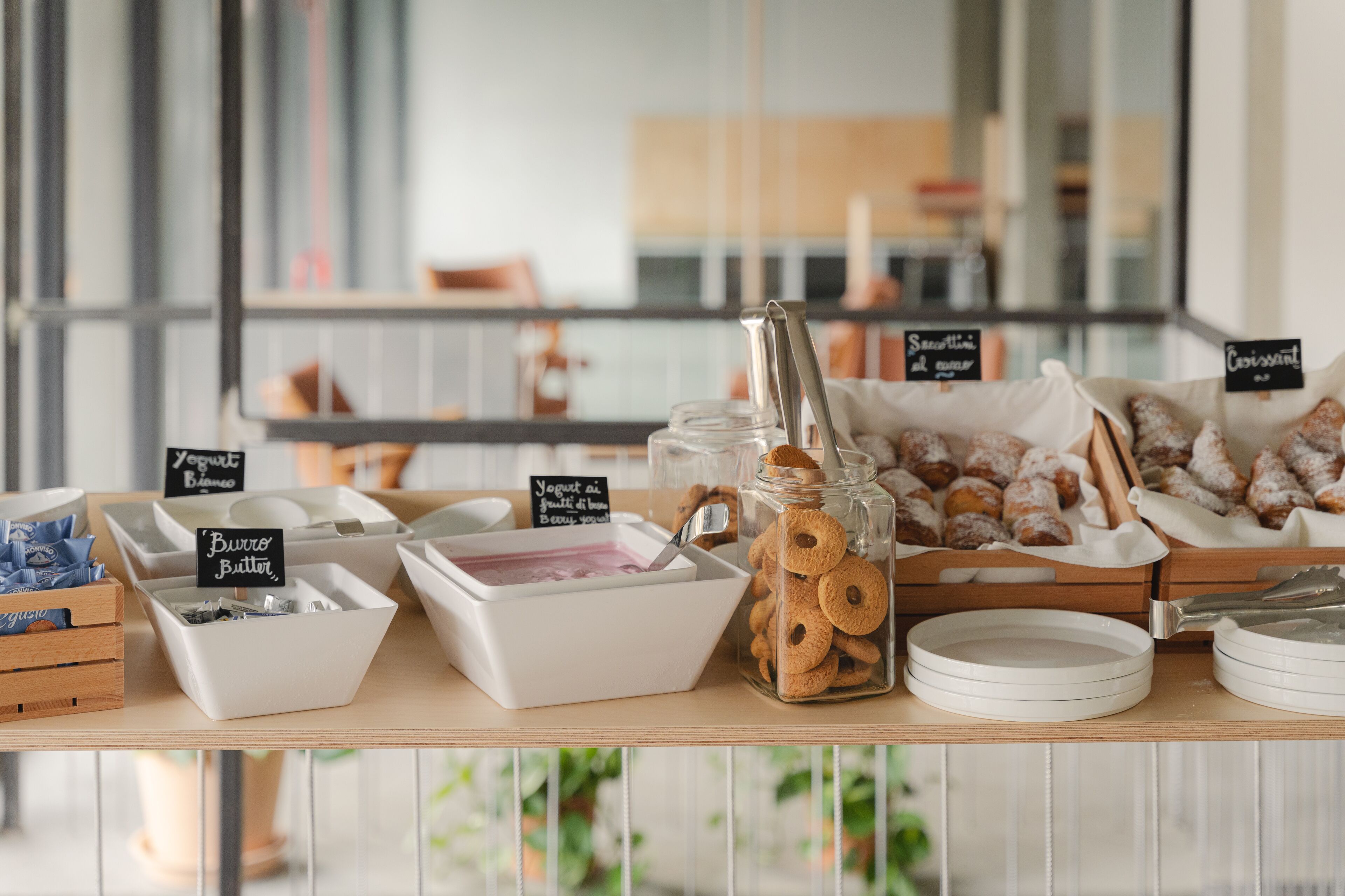 Una mesa de buffet con recipientes etiquetados de yogur, mantequilla y bollería.
