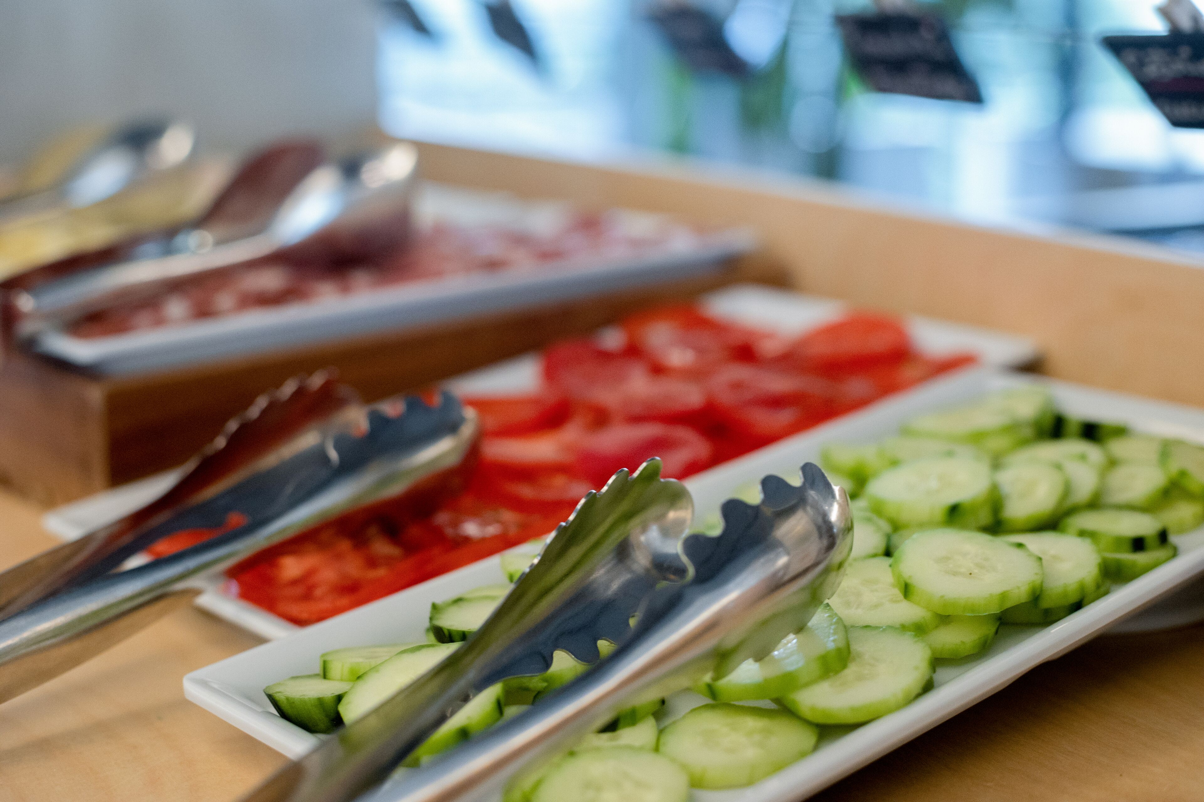 A buffet table with various food items including sliced cucumbers, tomatoes, and a container of red sauce.