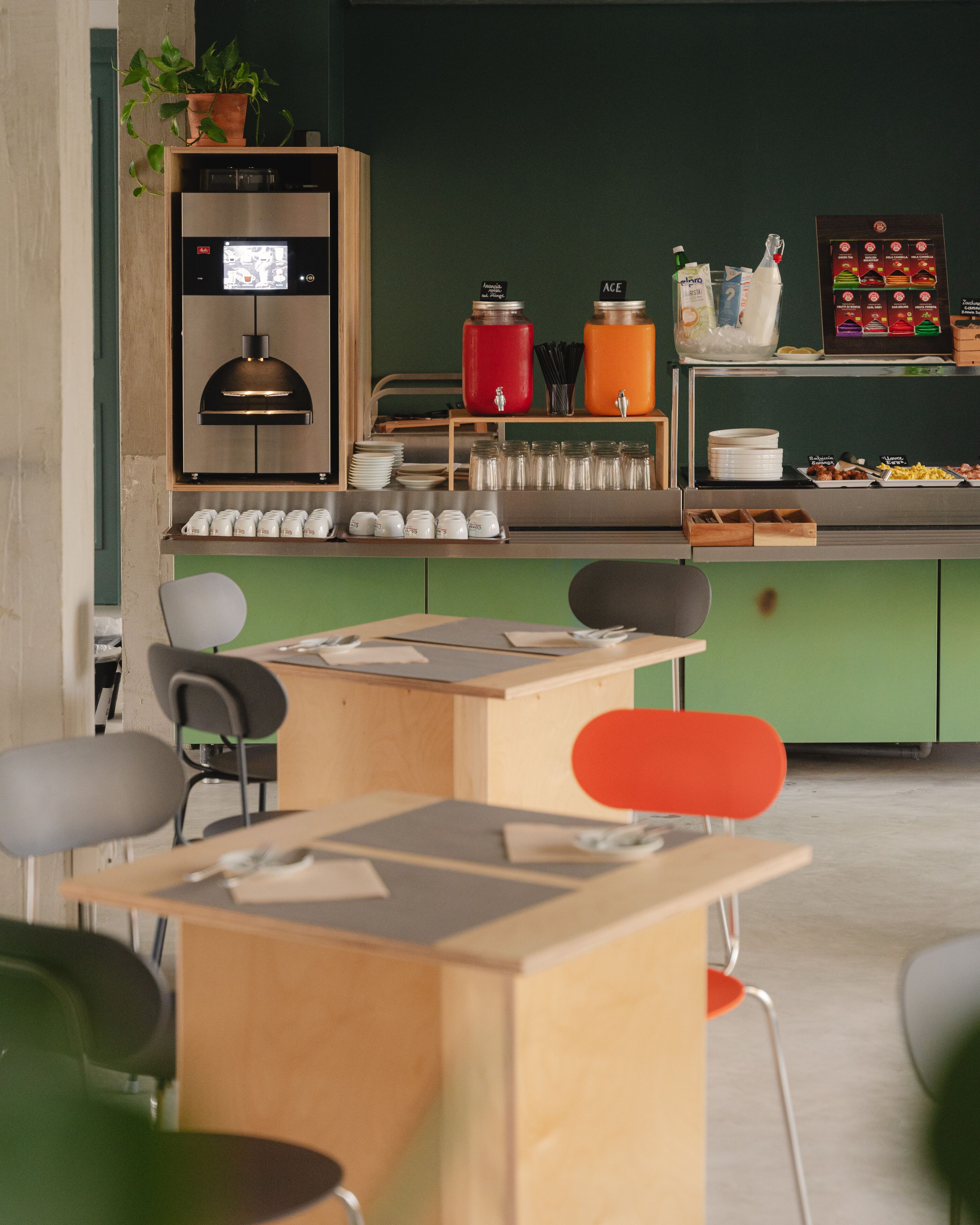 Una cocina moderna con una cafetera, un hervidor y diversos alimentos sobre la encimera. Se observan sillas y una mesa en primer plano.