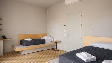 A modern hotel room with a checkered floor, a wooden bed frame, a desk with a laptop, and a door with a handle.