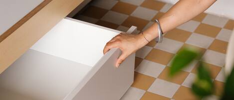 A hand opening a white drawer with a wooden frame in a room with a checkered floor.