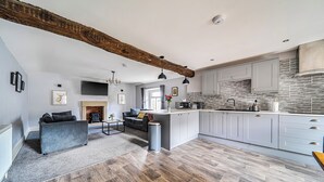 A spacious living area with a sofa, a fireplace, and a kitchen with white cabinets and a herringbone tile backsplash. - Cosy Apartment Above Village Pub (Buxton)