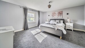 A bedroom with a bed, nightstands, a lamp, a painting, and a window with curtains. - Cosy Apartment Above Village Pub (Buxton)