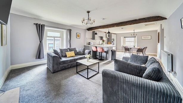 A modern living room with a sofa, armchairs, a coffee table, and a dining area with chairs. - Cosy Apartment Above Village Pub (Buxton)