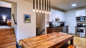 A modern kitchen with white cabinets, a wooden dining table, and a staircase leading to another room.