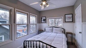 A bedroom with a bed, two bedside tables, a ceiling fan, and large windows.