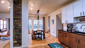 A modern kitchen with wooden cabinets, a stone accent wall, and a dining area with a table and chairs.