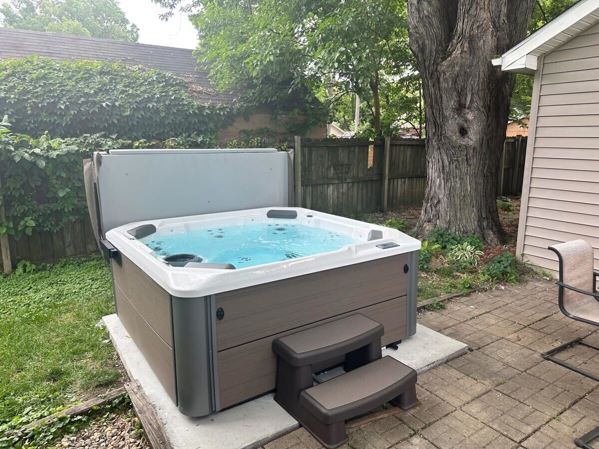 A hot tub with a step for access, surrounded by a wooden fence and a tree.