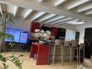 Una cocina moderna con armarios rojos, una zona de bar con taburetes y una pantalla grande que muestra un código QR.
