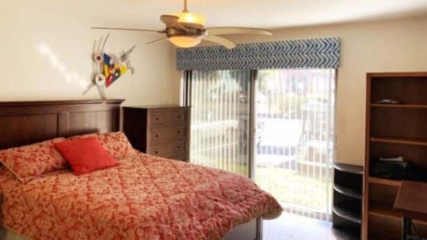 Een slaapkamer met een bed, een plafondventilator, een raam met uitzicht en een boekenkast.