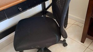 Een zwarte kantoorstoel met wielen, geplaatst voor een bureau met een houten blad en zwarte lades.