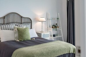 Une chambre à coucher bien rangée, avec un lit, des oreillers, une table de chevet, une lampe, une échelle et une étagère ornée d’objets décoratifs.