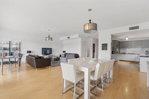 Moderni olohuone, jossa on ruokailutila, sohva, televisio ja keittiö.