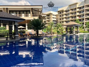 A hotel with a swimming pool, lounge chairs, and a pavilion.