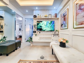 A modern living room with a flat-screen TV, white sofas, a coffee table, and a fireplace.