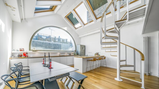 A modern kitchen with a large island, a dining area with a table and chairs, and a spiral staircase. - Unique Light-Filled Three-Bedroom Mews House (london)