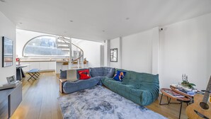 A modern living room with a curved grey sofa, a green sofa, a wooden coffee table, and a guitar. - Unique Light-Filled Three-Bedroom Mews House (london)