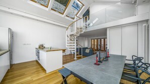 A modern kitchen with a dining area, wooden flooring, and a staircase leading to an upper level. - Unique Light-Filled Three-Bedroom Mews House (london)