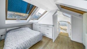 A bedroom with a skylight, a bed, a dresser, and a view of the city through the skylight. - Unique Light-Filled Three-Bedroom Mews House (london)