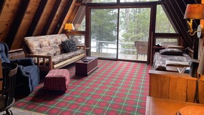 A cozy loft bedroom with a large window, a plaid carpet, and a wooden ceiling.