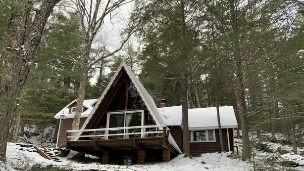 A cabin with a triangular roof, wooden deck, and a small porch.