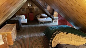 A cozy attic bedroom with two beds, a wooden dresser, and a red cabinet.