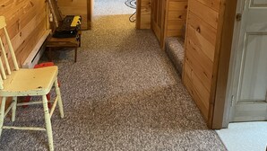A wooden interior hallway with a carpeted floor, a wooden bench, and a door leading to another room.