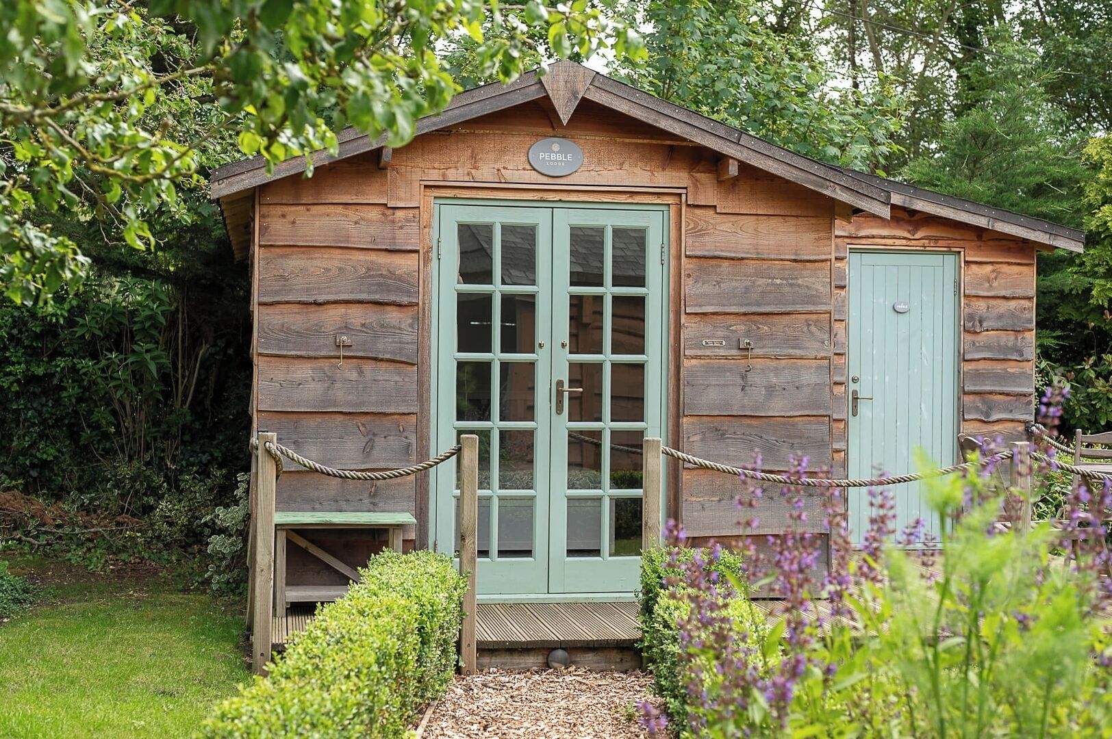 Una cabaña de madera con puerta verde, un pequeño porche y un cartel sobre la puerta.