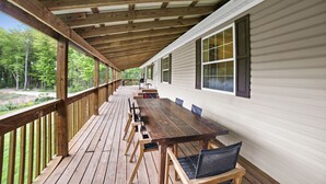 A covered wooden deck with a long table and chairs, surrounded by white siding walls.