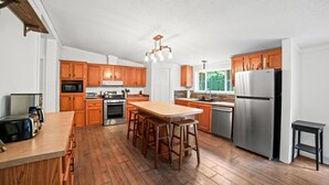 A modern kitchen with wooden cabinets, a stainless steel refrigerator, and a central island with bar stools.