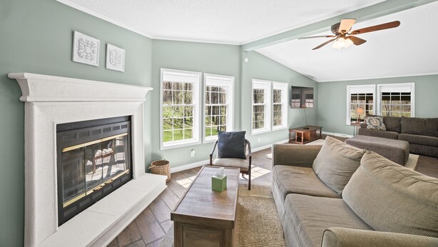A living room with a fireplace, large windows, a ceiling fan, and a sectional sofa.
