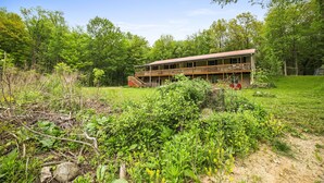 A two-story house with a balcony, surrounded by a natural landscape with trees and greenery.