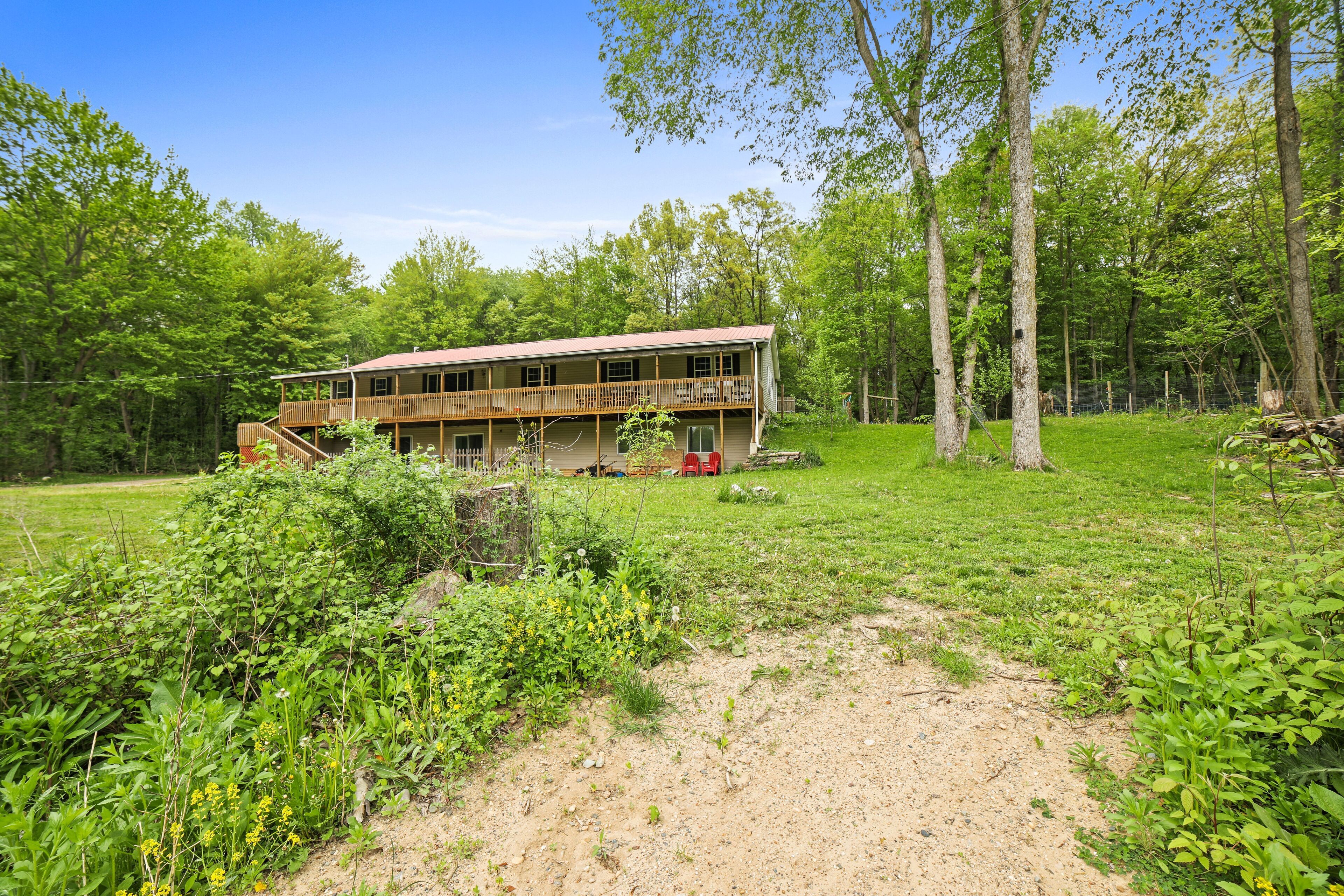 A two-story wooden cabin with a balcony, surrounded by a grassy field and dense trees.
