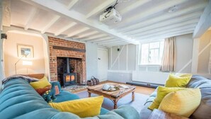 A cozy living room with a brick fireplace, a large blue sofa, and a wooden coffee table. - Ivy House Mells (Halesworth)