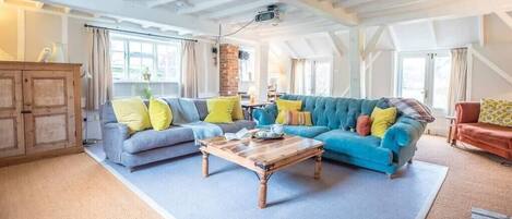 A cozy living room with a wooden coffee table, two sofas with colorful cushions, and a rustic wooden cabinet.