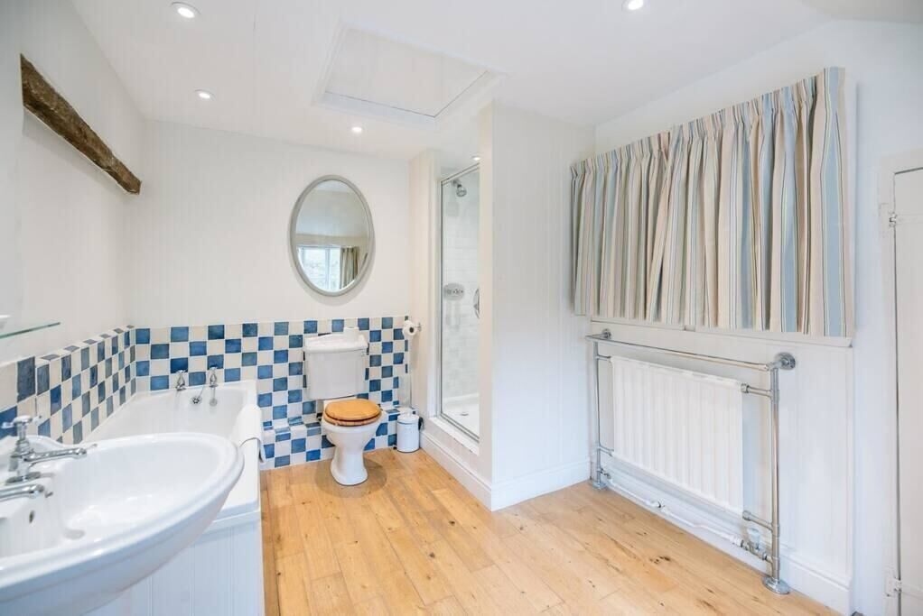 A bathroom with a checkered tile backsplash, a white sink, a wooden toilet, and a shower enclosure.