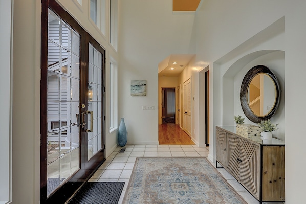 A hallway with a wooden door, a blue vase, a patterned rug, a mirror, and a cabinet.