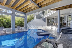 Una piscina exterior moderna con techo de madera, rodeada de sillones de descanso y una escalera que conduce a una zona cubierta.