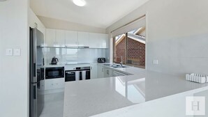 Een moderne keuken met witte kasten, roestvrijstalen apparatuur en een groot raam met uitzicht op een bakstenen muur.