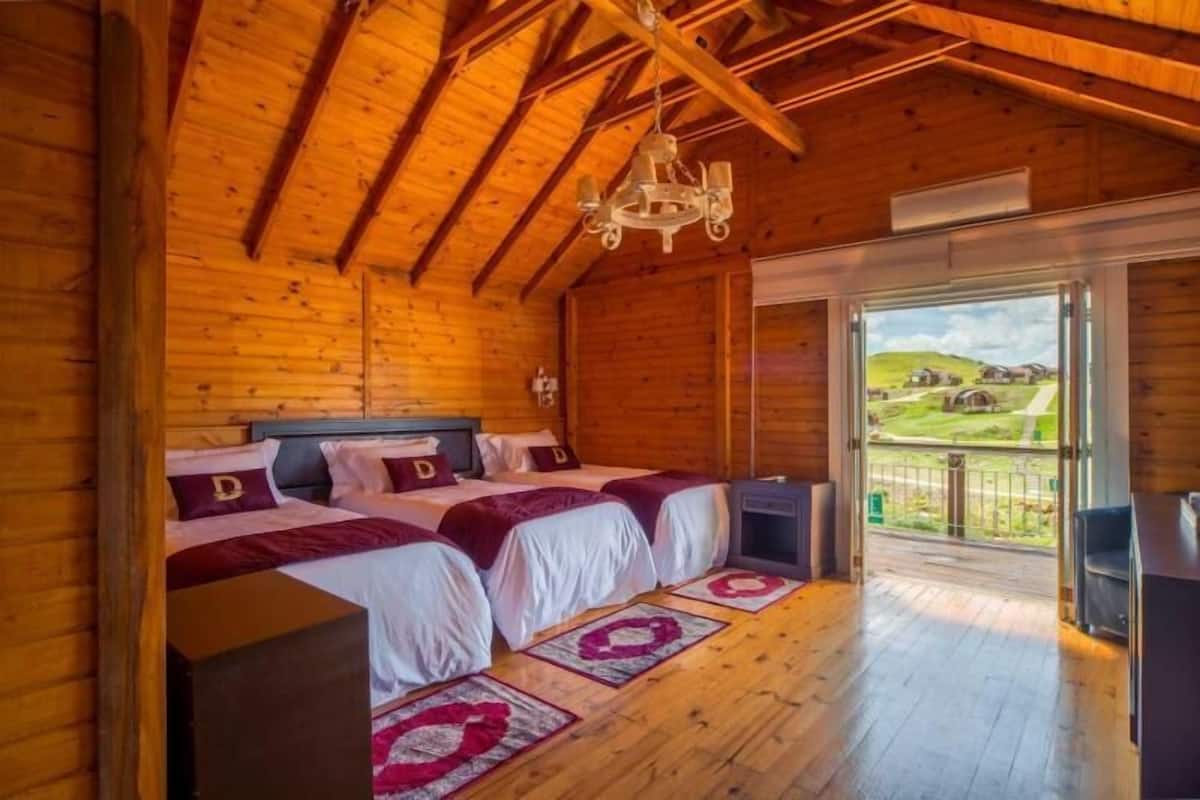 Un dormitorio de cabaña de madera con una cama grande, una araña y un balcón con vistas al campo.