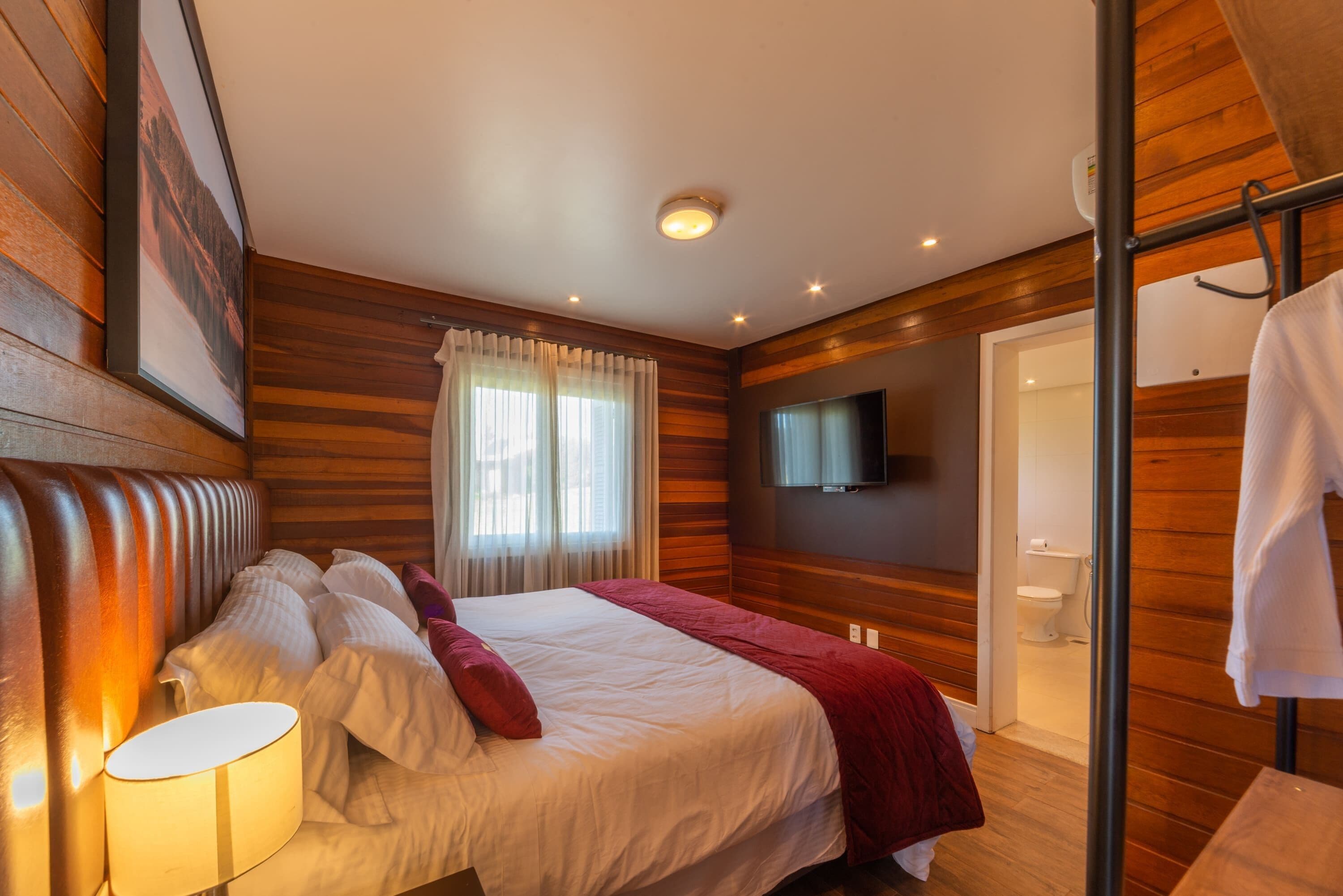 Un dormitorio con cama, televisor y baño visible a través de una puerta abierta.