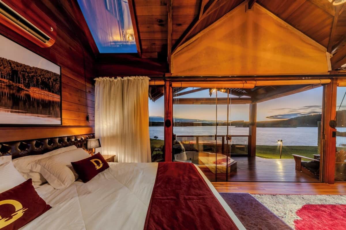 Un dormitorio con una cama grande, vista a un lago y techo de madera.