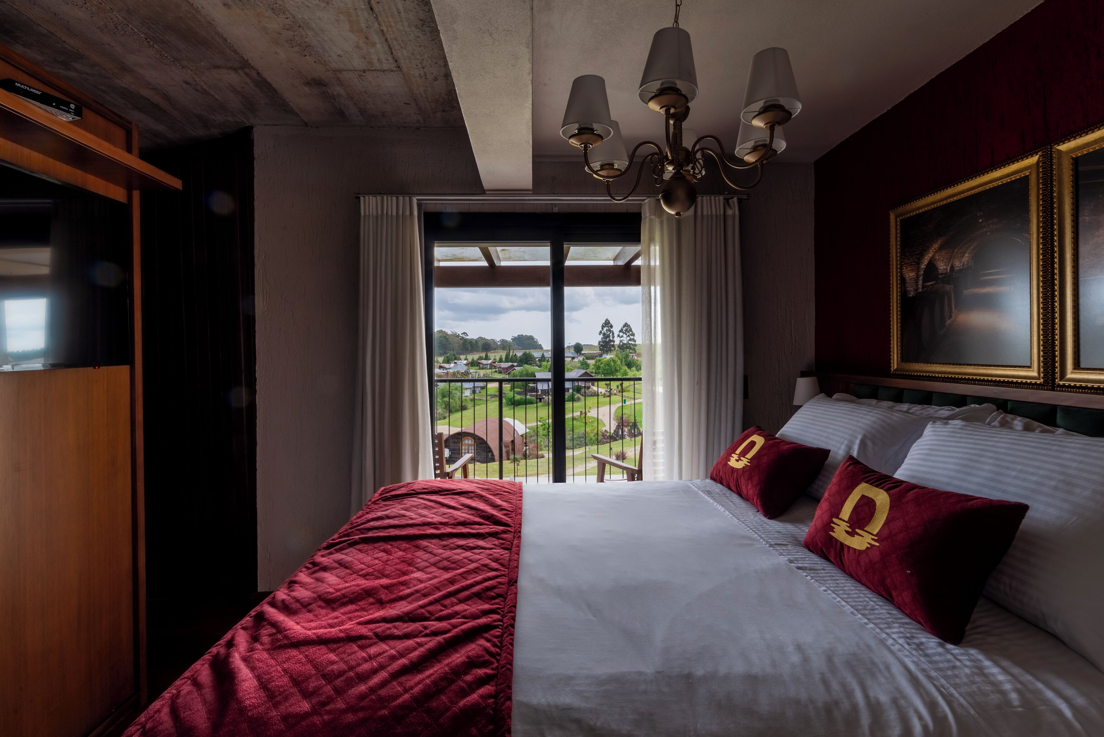 Habitación de hotel con una cama grande, una araña, vistas al exterior y un cuadro en la pared.