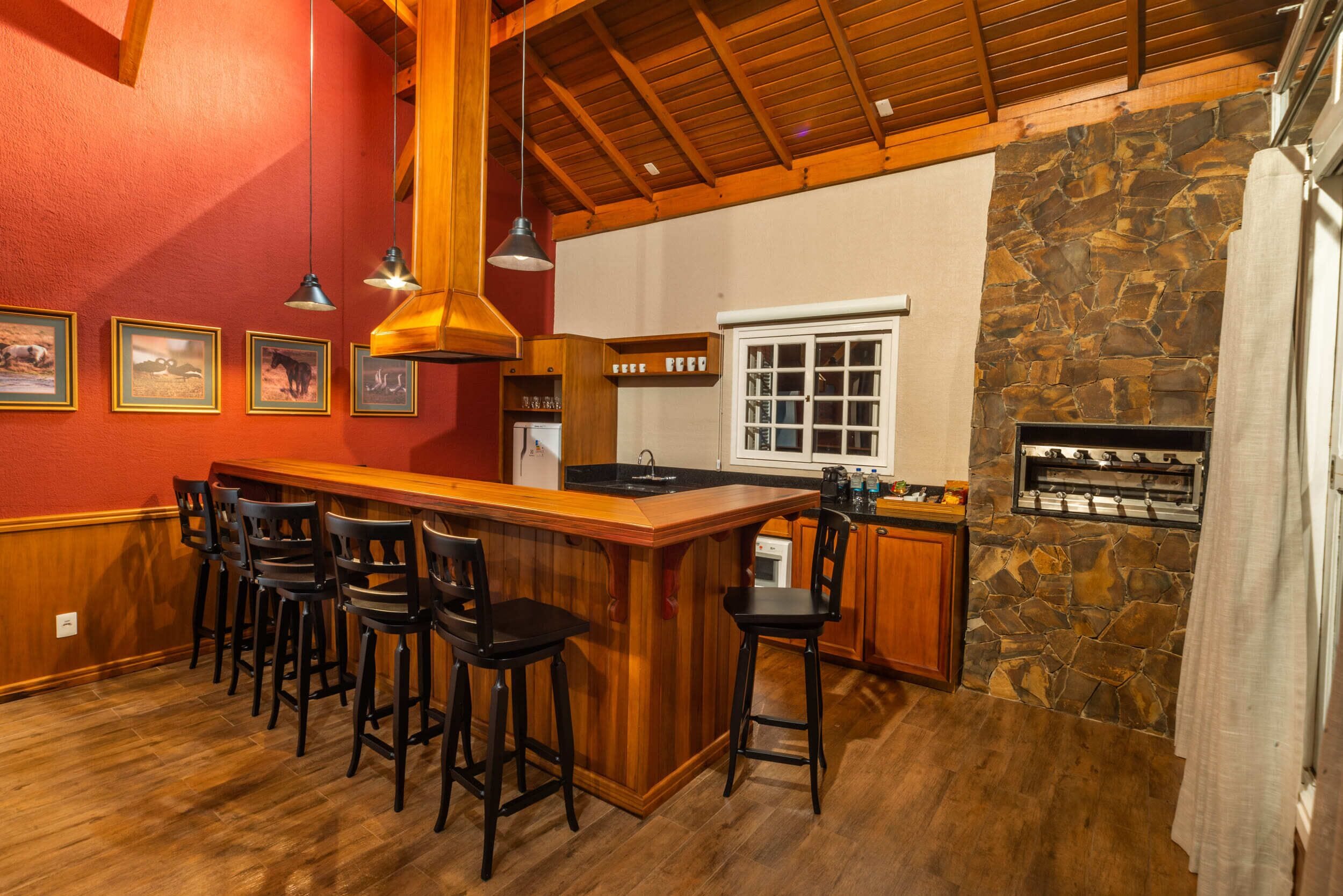 A kitchen with a bar area, wooden ceiling, stone wall, and bar stools.