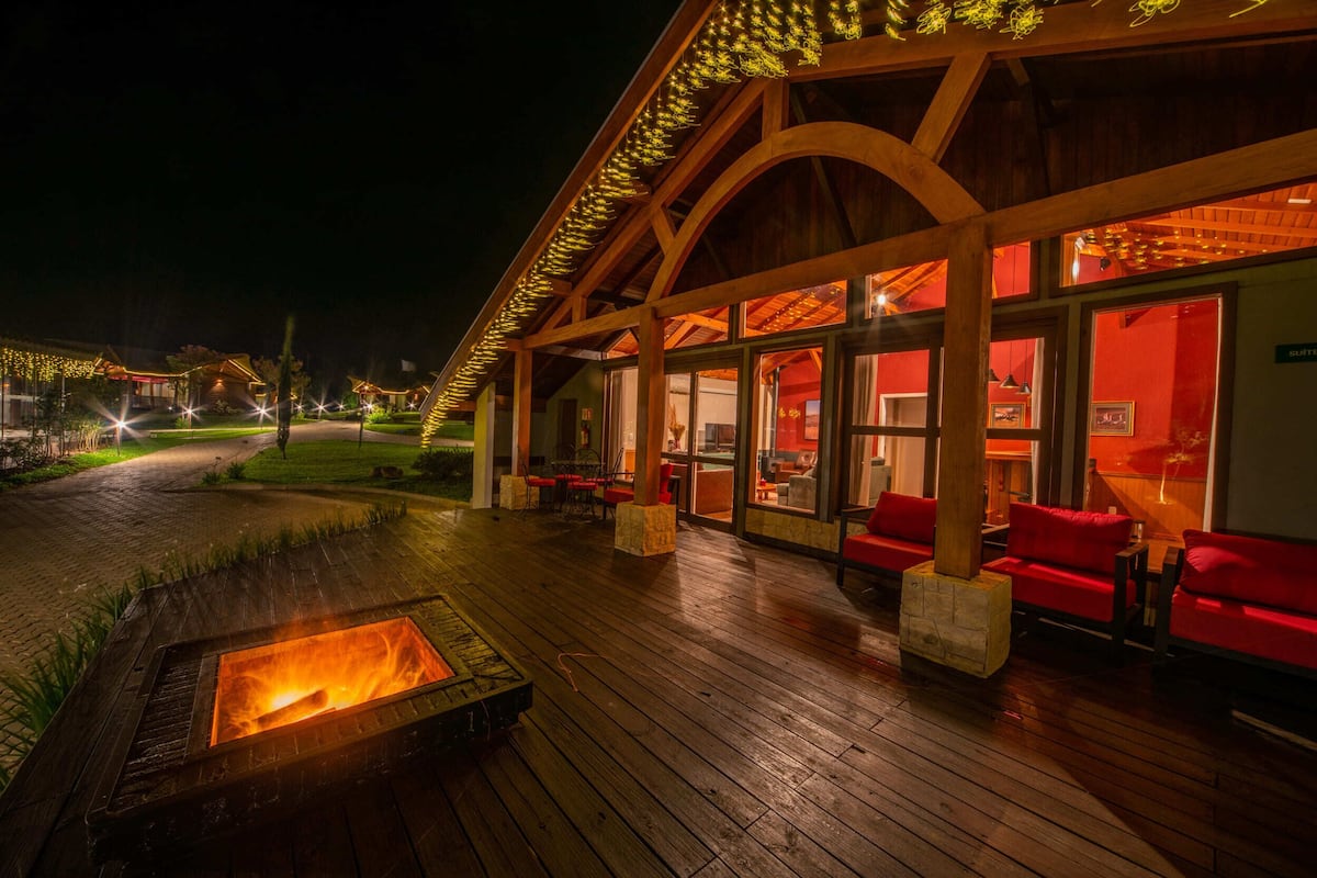 Una terraza de madera con un pozo de fuego, asientos rojos y una zona cubierta con paredes de vidrio.